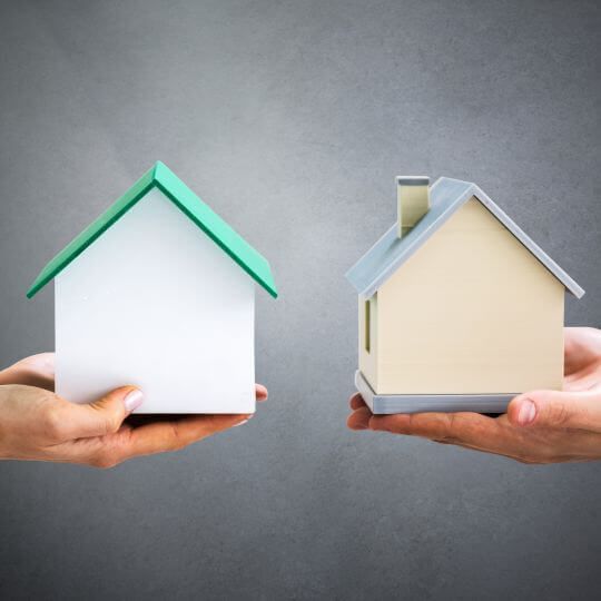 2 paar handen 1 links en 1 rechts waarbij beiden een huisje vasthouden. Bij Woningruil ruil je biedt ieder zijn huis aan de ander aan om te ruilen.